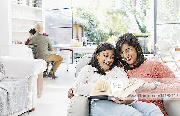 Mutter und Tochter lesen ein Buch im Wohnzimmer