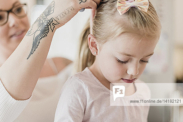 Mutter mit Tattoos  die das Haar ihrer Tochter fixiert