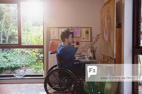 Männlicher Künstler im Rollstuhl malt im Kunstatelier
