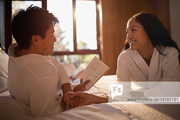 Paar in Bademänteln liest Buch im Bett