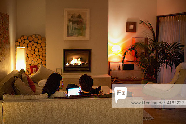 Couple using digital tablet on living room sofa facing fireplace