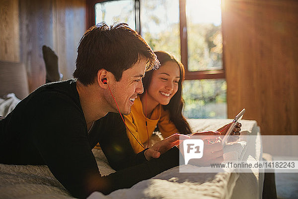 Happy couple with headphones sharing digital tablet on bed