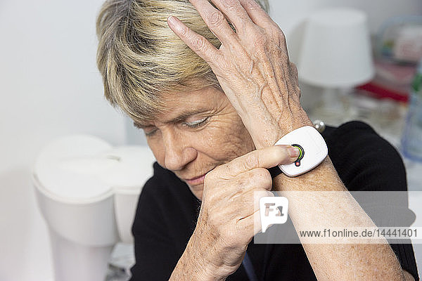Ältere Frau mit einem medizinischen Alarmsystem um ihr Handgelenk.