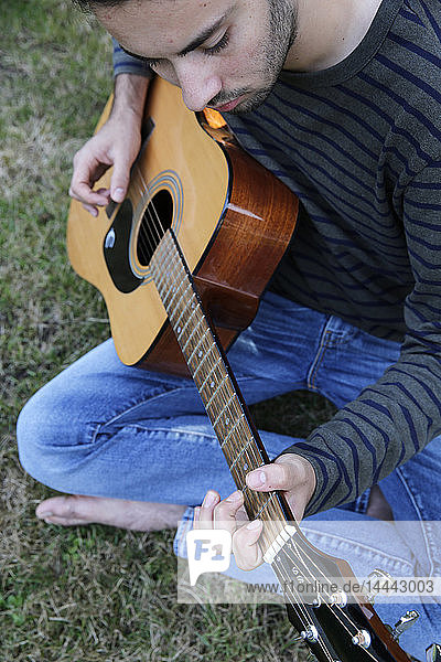 Junger Mann spielt Gitarre in einem Garten. Frankreich.