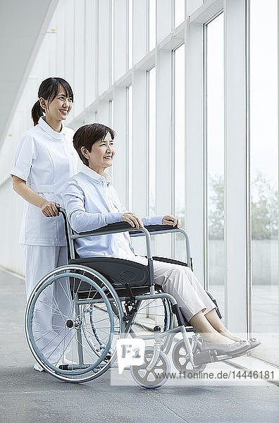 Junge japanische Pflegerin kümmert sich um älteren Patienten