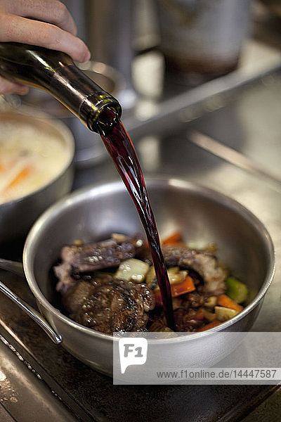 Wine being added to a pan with meat and vegetables