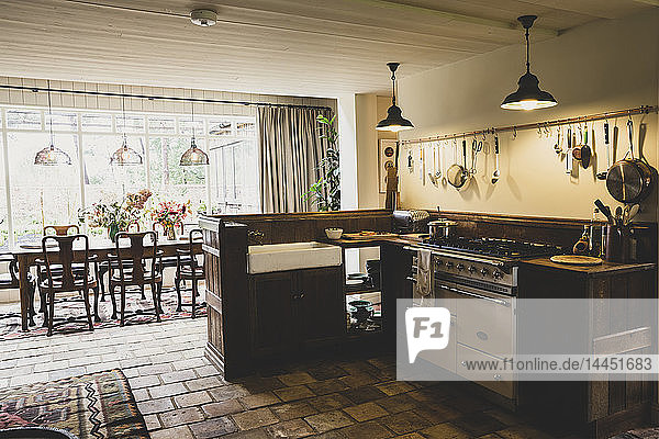 Innenansicht der Küche mit Steinfliesenboden  Herd und Butlerspüle  offener Grundriss zum Wintergarten mit antikem Holztisch und Stühlen.