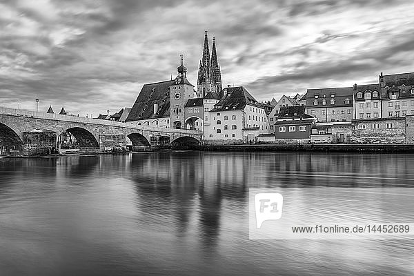 Mittelalterliche Steinbogenbrücke über die Donau mit historischen Gebäuden und gotischer Kathedrale in der Ferne  Regensburg  Deutschland.