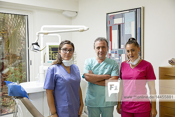 Ein Zahnarzt und seine 2 Assistentinnen in bunten Blusen in seiner Zahnarztpraxis.