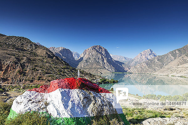 Iskanderkul-See mit einem großen  in den Farben der tadschikischen Flagge bemalten Felsen im Vordergrund  Fächergebirge  Tadschikistan  Zentralasien