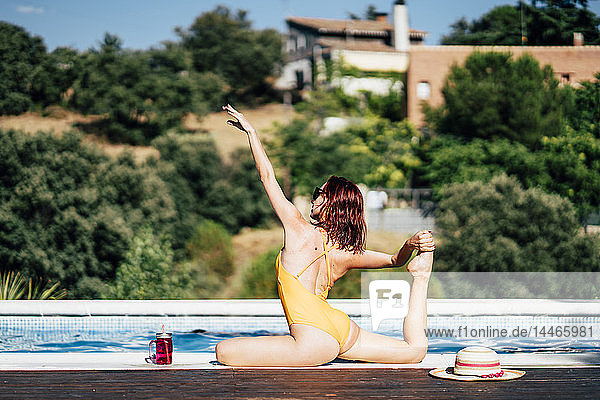 Hübsche Frau im Badeanzug praktiziert Yoga am Poolrand
