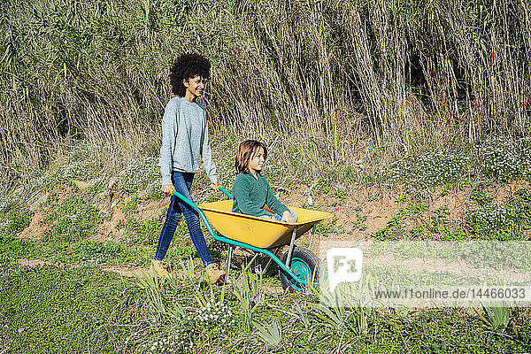 Father walking on a dirt track  pushing wheelbarrow  with his son sitting in it