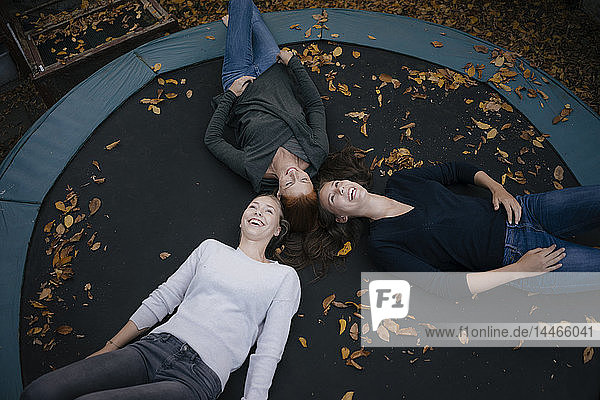 Glückliche Mutter mit zwei Mädchen im Teenageralter, die im Herbst auf dem Trampolin liegen