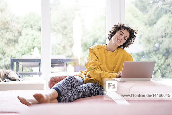 Smiling woman using laptop on couch at home