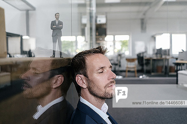 Geschäftsmann sitzt in seinem Büro mit seinem 3D-Portrait hinter einer Glasscheibe