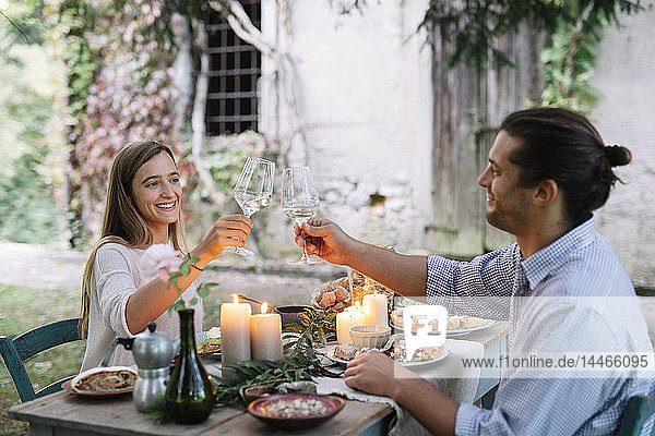 Couple having a romantic candlelight meal next to a cottage clinking wine glasses
