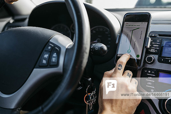 Nahaufnahme eines Mannes mit tätowierter Hand beim Autofahren mit einem Mobiltelefon als Navigationssystem