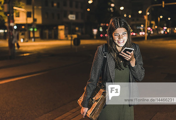Lachende junge Geschäftsfrau mit Ledertasche nachts am Telefon