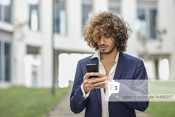 Young businessman with curly hair text messaging