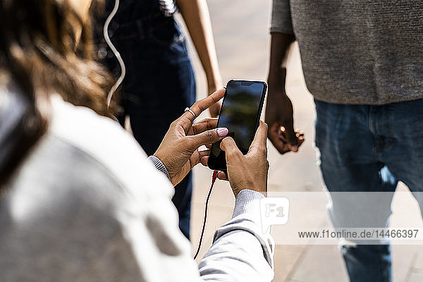 Junge Frau mit Kopfhörern  die ein Smartphone benutzt  mit Freunden in der Nähe