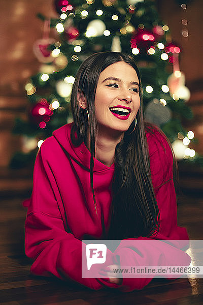 Porträt eines lachenden Teenagers  der vor einem Weihnachtsbaum auf dem Boden liegt