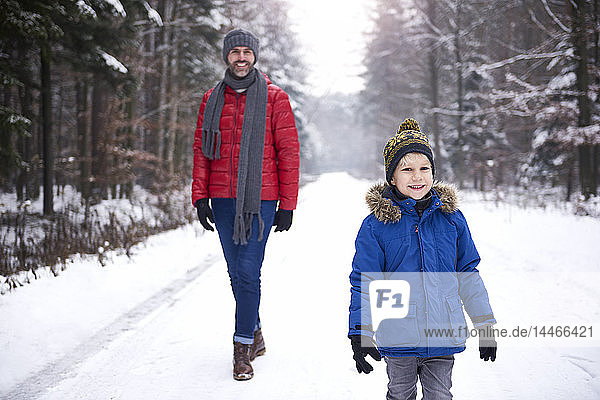 Portrait of happy little boy strolling together with his father in winter forest