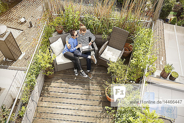 Young couple relaxing on their balcony  sitting on couch  using laptop