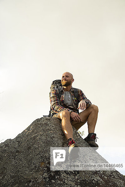 Spanien  Andalusien  Tarifa  lächelnder Mann auf einer Wanderung  der auf einem Felsen sitzend eine Pause macht