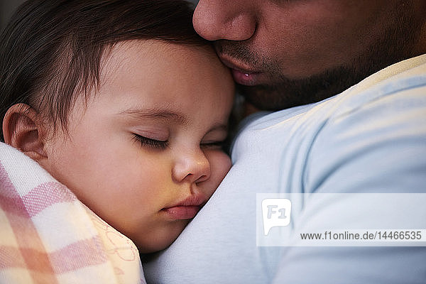 Close-up of father kissing sleeping baby girl
