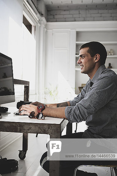 Junger Mann sitzt am Schreibtisch und benutzt Computer