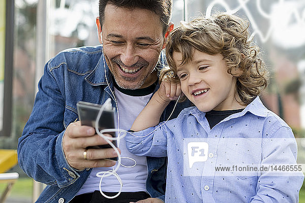 Glücklicher Vater und Sohn teilen sich Handy und Kopfhörer