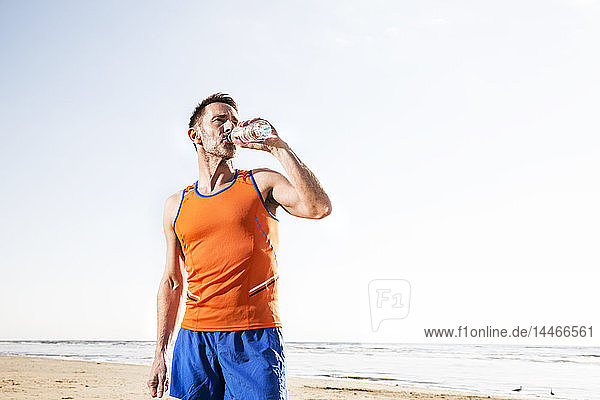 Sportler  der am Strand aus der Flasche trinkt