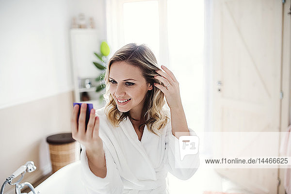 Smiling woman in bathrobe looking in mirror in the morning at home