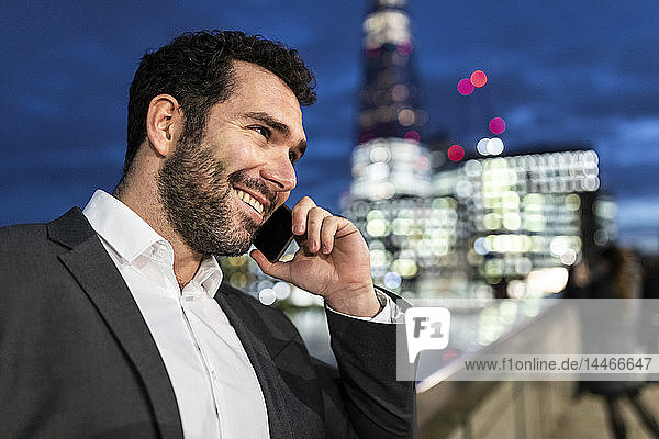 Großbritannien  London  Porträt eines lächelnden Geschäftsmannes  der nachts beim Pendeln telefoniert