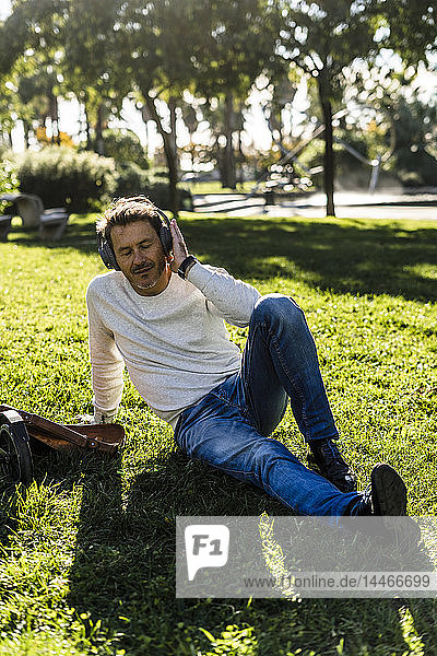 Casual businessman taking a break in a prak  sitting on grass  listening music