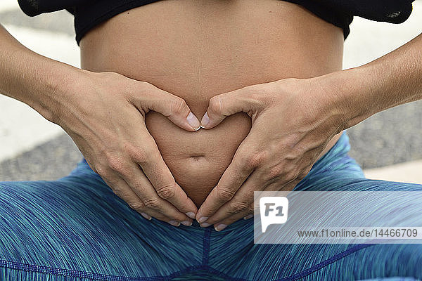 Nahaufnahme einer schwangeren Frau  die ein Herz um ihren Bauch formt