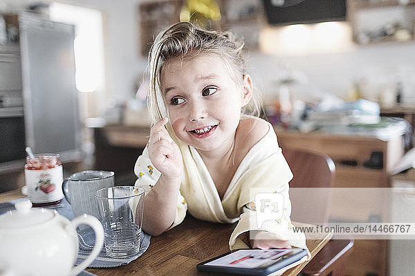 Portrait of smiling little girl with smartphone in the kitchen