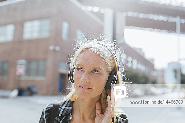 USA  New York City  Brooklyn  Porträt einer jungen Frau  die in der Stadt mit Kopfhörern Musik hört