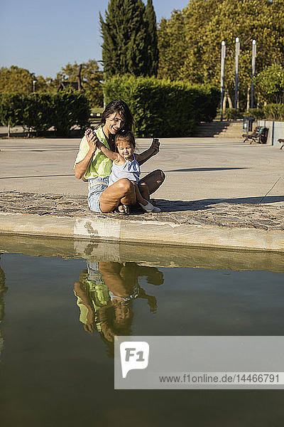 Glückliche Mutter mit Tochter an einem Pool in einem Park