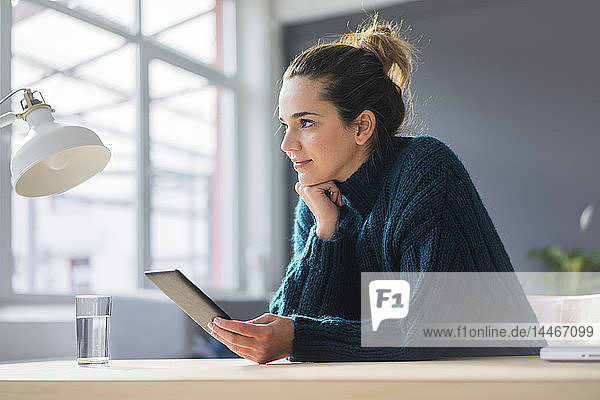 Porträt einer lächelnden Frau  die mit einem digitalen Tablett am Schreibtisch sitzt und in die Ferne schaut