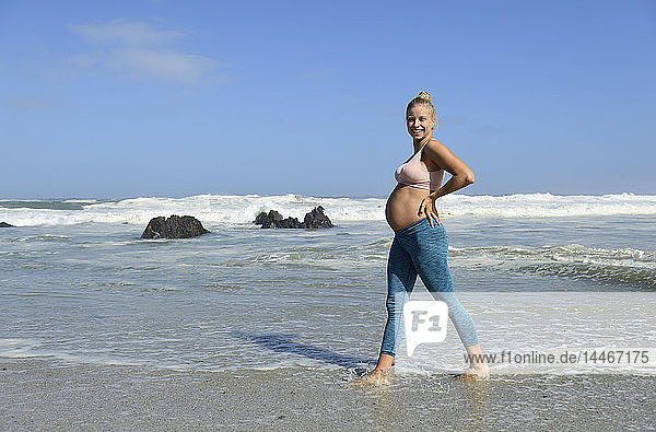 Porträt einer glücklichen schwangeren Frau am Strand  die im Meer watet