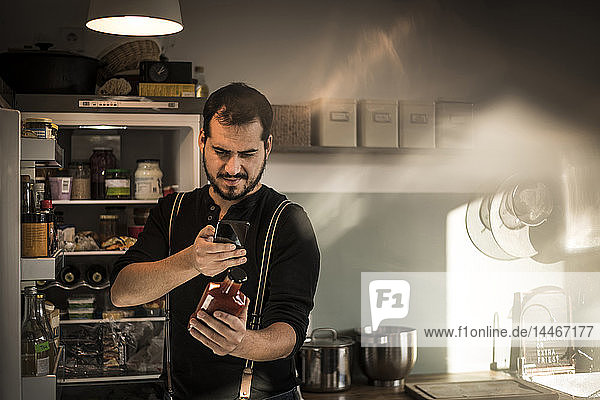 Man standing in front of fridge  scanning sauce bottle with his smartphone