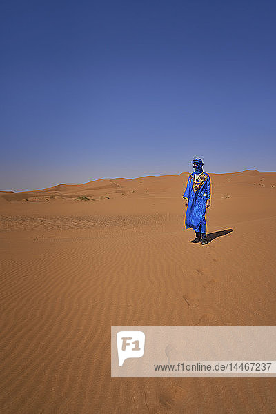 Morocco  man wearing blue kaftan and turban standing on desert dune