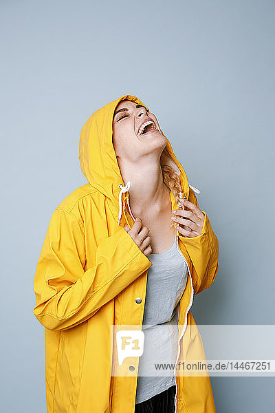Lachende junge Frau in gelbem Regenmantel vor blauem Hintergrund