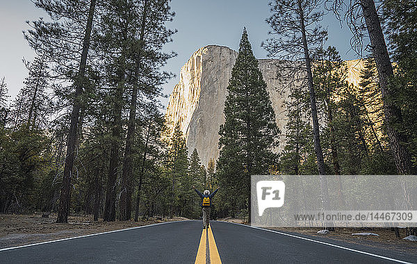 USA  California  Yosemite National Park  man with raised arms on road with El Capitan in background