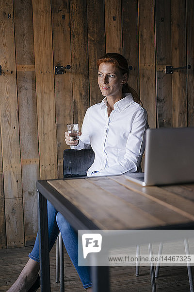 Geschäftsfrau sitzt am Schreibtisch mit einem Glas Wasser und einem Laptop