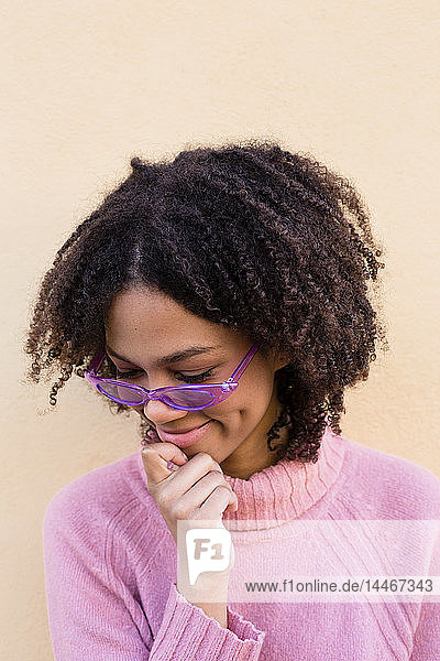 Porträt einer lächelnden jungen Frau mit rosa Pullover und lila Sonnenbrille