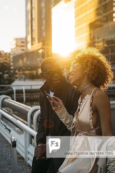 Glückliches Paar mit Mobiltelefonen in der Stadt bei Sonnenuntergang