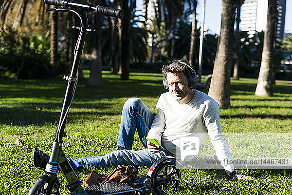 casual businessman sitting on grass in a park  using smartphone and headphones