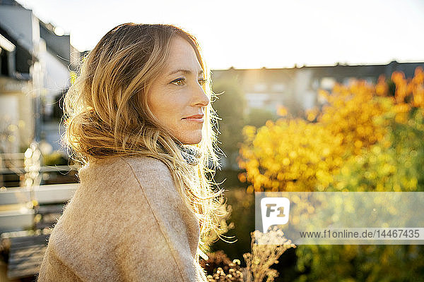 Blonde reife Frau genießt sonnigen Herbsttag auf dem Balkon